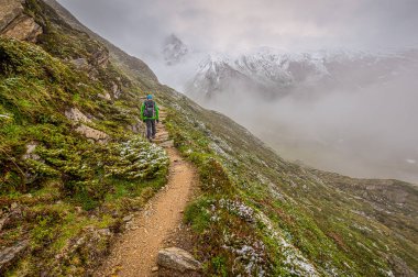 Bir yürüyüşçü sisli arka planda güzel bir dağla yamaçta yürüyor.