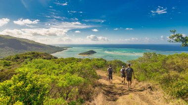 Dağdan manzara - güzel bir vadi, bulutlar ve okyanus. Mauritius 'un ana sembolü olan Le Morne Brabant dağında yürüyen üç yürüyüşçü..