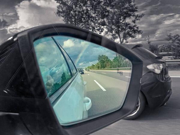 rearview car driving mirror view at a colorful rainbow while the surrounding is black and white, kind of colorkey
