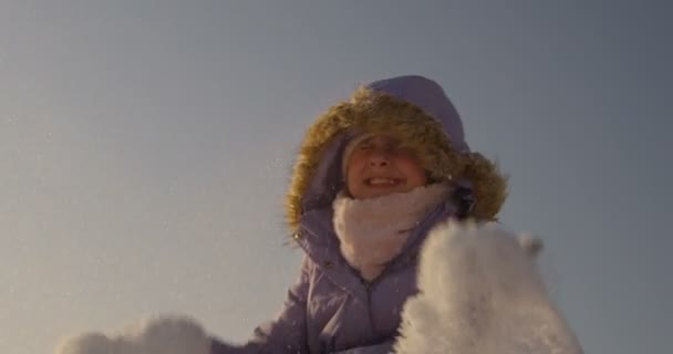 座っているとスローモーションで晴れた日に青空に雪を投げる小さな女の子歓喜 — ストック動画