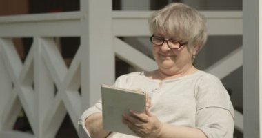 Kırmızı Kamera'da çekilen Terrasse Evi Veranda'da Güneşli Günde Güneşli Günde Gözlüklü Tablet Kullanan Kıdemli Kadın Portresi