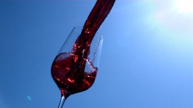 Kırmızı Şarap Yavaş Hareket Arka Planda Mavi Gökyüzü ve Sunshine ile Bir Kadeh için Pouring olduğunu