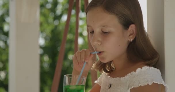 夏の日のクローズアップで楽しい笑顔を持って裏庭のテラスに座ってカクテルを飲む若い女の子 — ストック動画