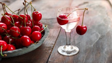 Kirsch ya da Kirschwasser. Bardakta alkollü vişne suyu ve eski, siyah bir tahta masada taze kiraz.