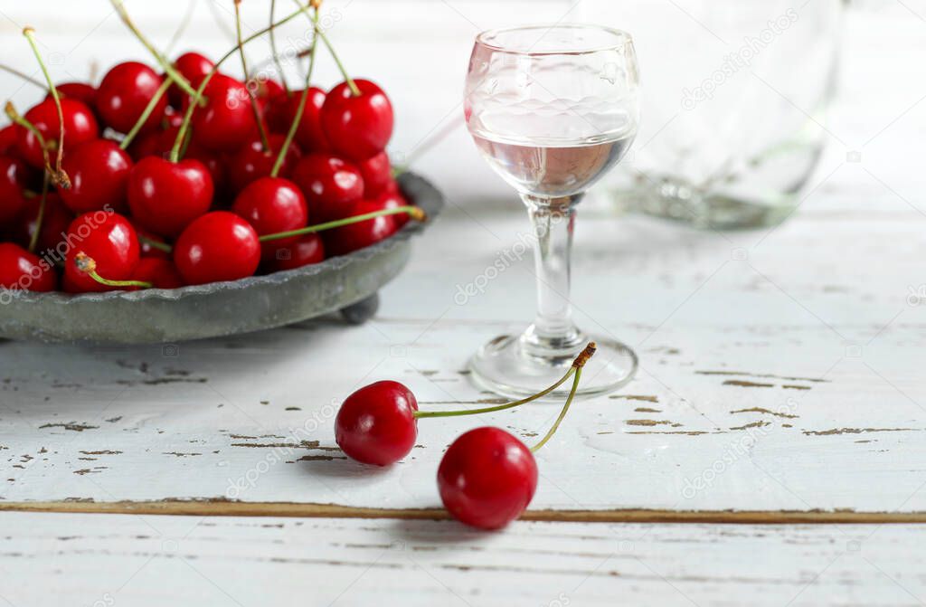 Strong alcoholic cherry drink Kirsch or Kirschwasser - in a glass and fresh cherry on the white wooden table