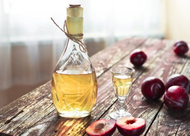 Geleneksel Balkan erik brendisi - rakija veya rakia slivovica şişede, sljivovica 'lı bir şarap kadehi ve gün ışığında ahşap zeminde taze erikler.