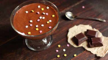 Bir kase çikolatalı mus, bir parça siyah çikolata ve eski koyu kahverengi masa arkasında bir çay kaşığı.