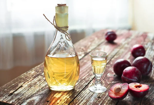 Traditional Balkan plum brandy - rakija or rakia slivovica in the bottle, a wineglass with sljivovica and fresh plums on the wooden background in daylight.