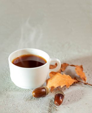 Bir fincan meşe palamudu sıcak kahve, meşe palamudu ve gri arka planda sarı meşe yaprakları. Kafeinsiz ev yapımı sıcak bir içecek.