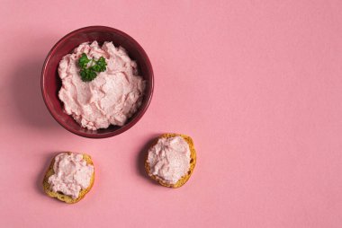Pembe arka planda, tarama ya da taramasalata soslu bir kase ve crostini.