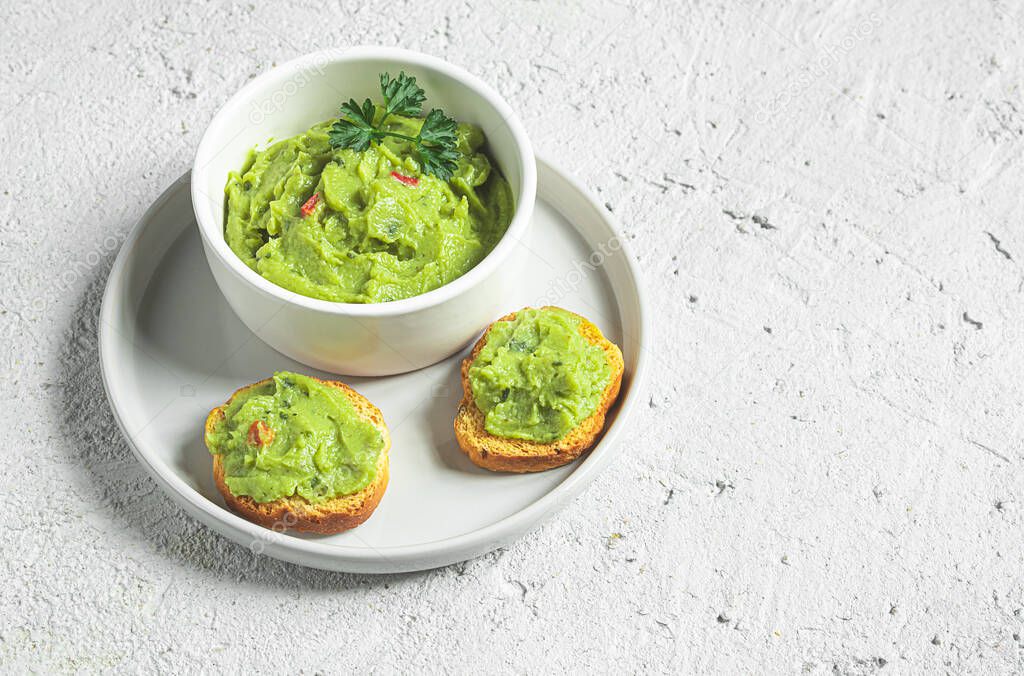 A white bowl and crostini or bruschetta with traditional mexican appetizer guacamole on the gray plate. Vegetarian snacks