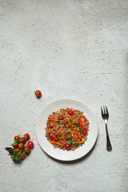 Sıcak karabuğday, domates, dolmalık biber, soğan, zeytinyağı ve gri arka planda beyaz bir tabakta farklı bitkiler içeren sebze salatası.