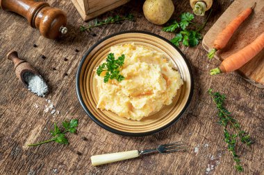 Patates, havuç ve koyu ahşap zeminde lezzetli yaban havucu püresi yapmak için malzemeyle ezilmiş yaban havucu. Vitamin ve mineral açısından zengin lezzetli ve sağlıklı vejetaryen yemekleri..