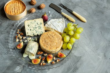Fransız peynirinin çeşitli çeşitleri - camembert, rokfor, brie peyniri, keçi peyniri ve üzümlü, incirli ve fındıklı gri arka planda. Üst görünüm, alanı kopyala