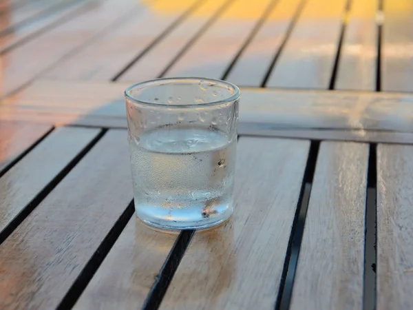 Glass with chilled drink covered with drops, on wooden table in cafe