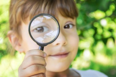 Çocuk bir büyüteç içine bakıyor. Arttır. seçici odak.