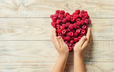 Bir kalp şeklinde bir çocuğun elinde ahududu vardır. Ev. Seçici odak.