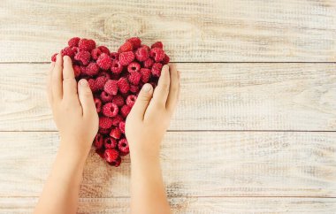 Bir kalp şeklinde bir çocuğun elinde ahududu vardır. Ev. Seçici odak.