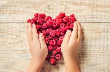 Bir kalp şeklinde bir çocuğun elinde ahududu vardır. Ev. Seçici odak.