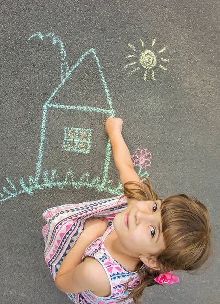 The child draws the house with chalk on the asphalt. Selective focus. draw.