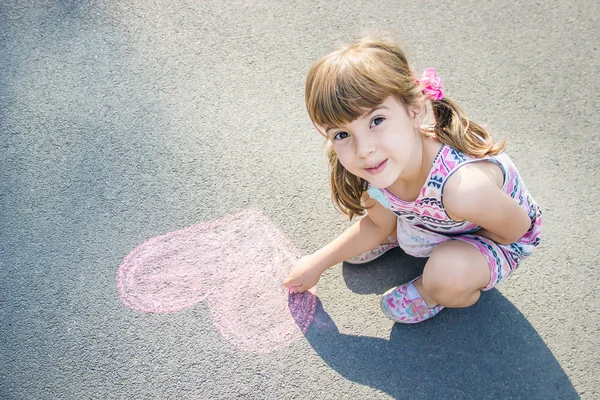 The child paints chalk on the asphalt heart. Selective focus. — Stock Photo, Image