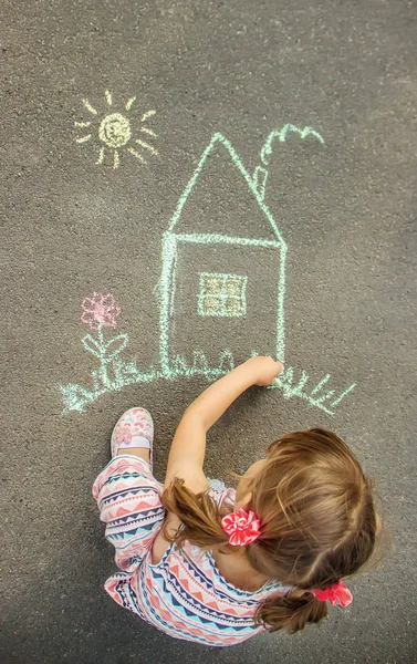 Das Kind zeichnet das Haus mit Kreide auf den Asphalt. Selektiver Fokus. — Stockfoto