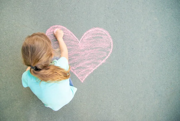A criança pinta giz no coração de asfalto. Foco seletivo . — Fotografia de Stock