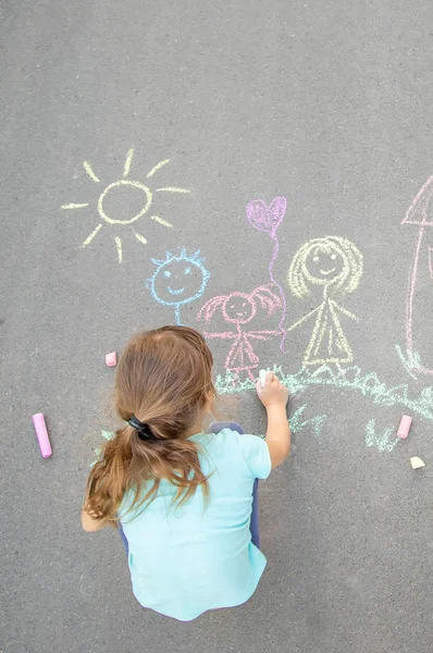 L'enfant dessine une famille sur le trottoir avec de la craie. Concentration sélective . — Photo