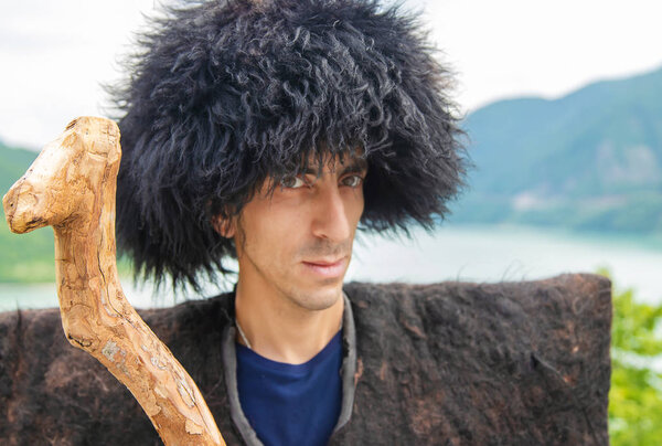 Georgian man in a beech costume on a background of mountains. Selective focus.