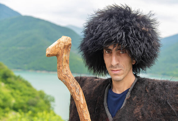 Georgian man in a beech costume on a background of mountains. Selective focus.