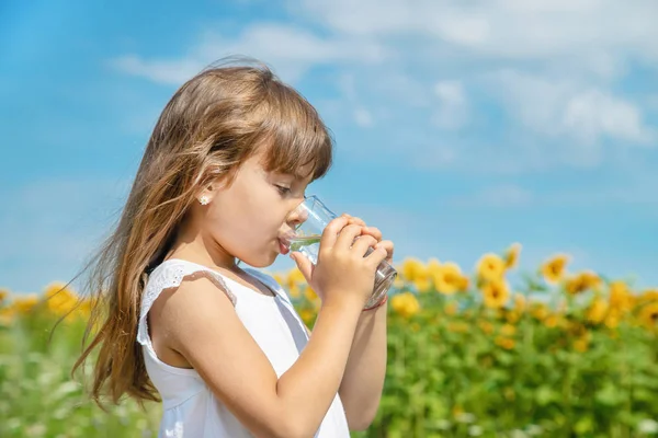 Ein Kind trinkt Wasser auf dem Hintergrund des Feldes. Selektiver Fokus. — Stockfoto