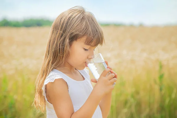 Un niño bebe agua en el fondo del campo. Enfoque selectivo . — Foto de Stock