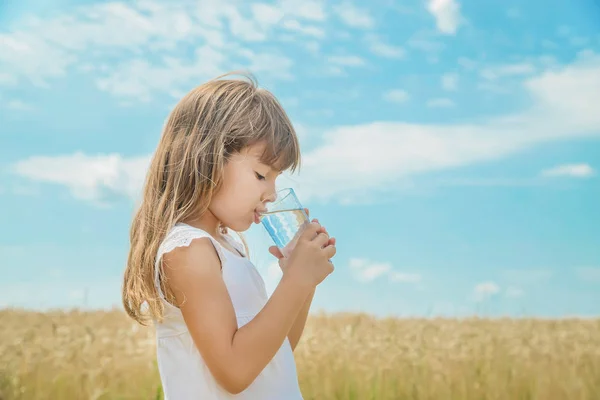 Un niño bebe agua en el fondo del campo. Enfoque selectivo . — Foto de Stock