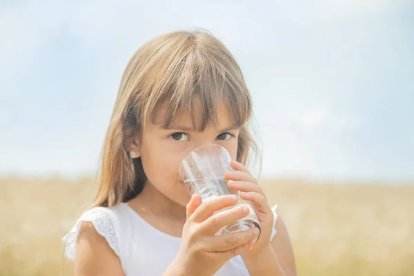 Ett barn dricker vatten på bakgrunden av fältet. Selektivt fokus. — Stockfoto