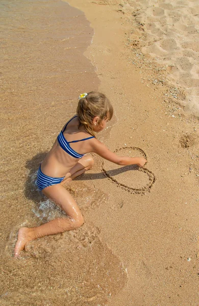 Dziecko rysuje w piasku na plaży. Selektywna koncentracja. — Zdjęcie stockowe
