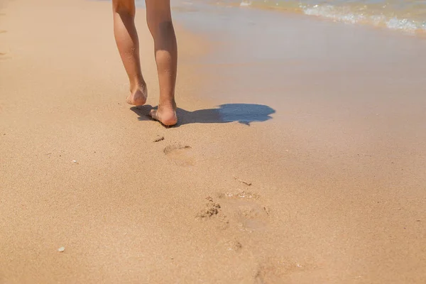 Çocuk kumda ayak izleri bırakarak plaj boyunca yürür. Seçici odaklama. — Stok fotoğraf