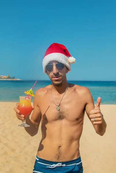 O homem de chapéu de Pai Natal está a descansar no mar. Bebe um cocktail. Foco seletivo . — Fotografia de Stock