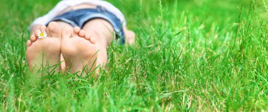 Yeşil çimlerin üzerinde papatya çayı olan çocuk ayakları. Seçici odaklanma. Doğa.