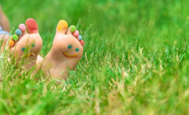 Yeşil çimlerin üzerinde gülümseyen boya desenli çocuk ayakları. Seçici odaklanma. Doğa.