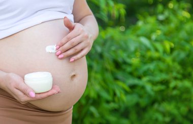 Gerilme izleri için kremi olan hamile bir kadın. Seçici odaklanma. Doğa.