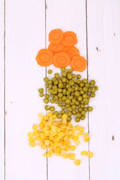 Corn, peas, carrots on a wooden background