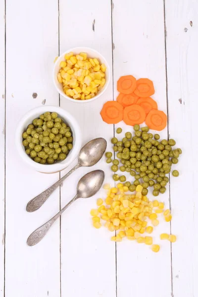 Corn, peas, carrots on a wooden background