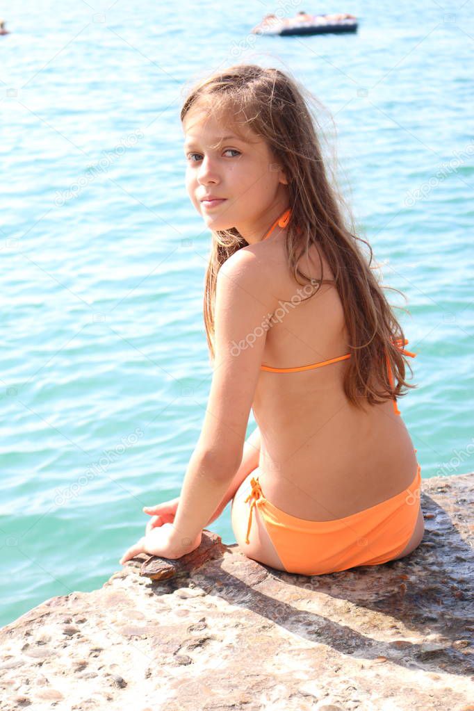 A girl in a bathing suit on the background of the sea. Girl sitting on a stone