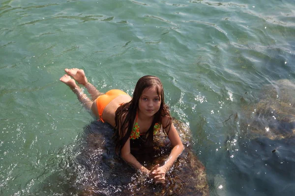女の子は海で泳いでいます 海の水の石に座っている女の子 — ストック写真