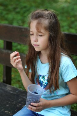 Kız bankta bir blueberry plastik bir kap vardır.