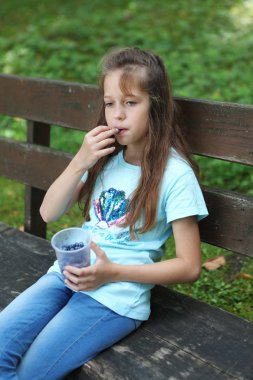 Kız bankta bir blueberry plastik bir kap vardır.
