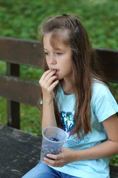 Kız bankta bir blueberry plastik bir kap vardır.