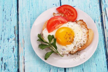 Bir dilim domates ve maydanoz ile beyaz ekmek üzerinde kızarmış yumurta