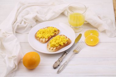 Beyaz ahşap bir masada portakal suyu ile iki tost üzerinde çırpılmış yumurta ile natürmort