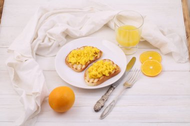 Beyaz ahşap bir masada portakal suyu ile iki tost üzerinde çırpılmış yumurta ile natürmort